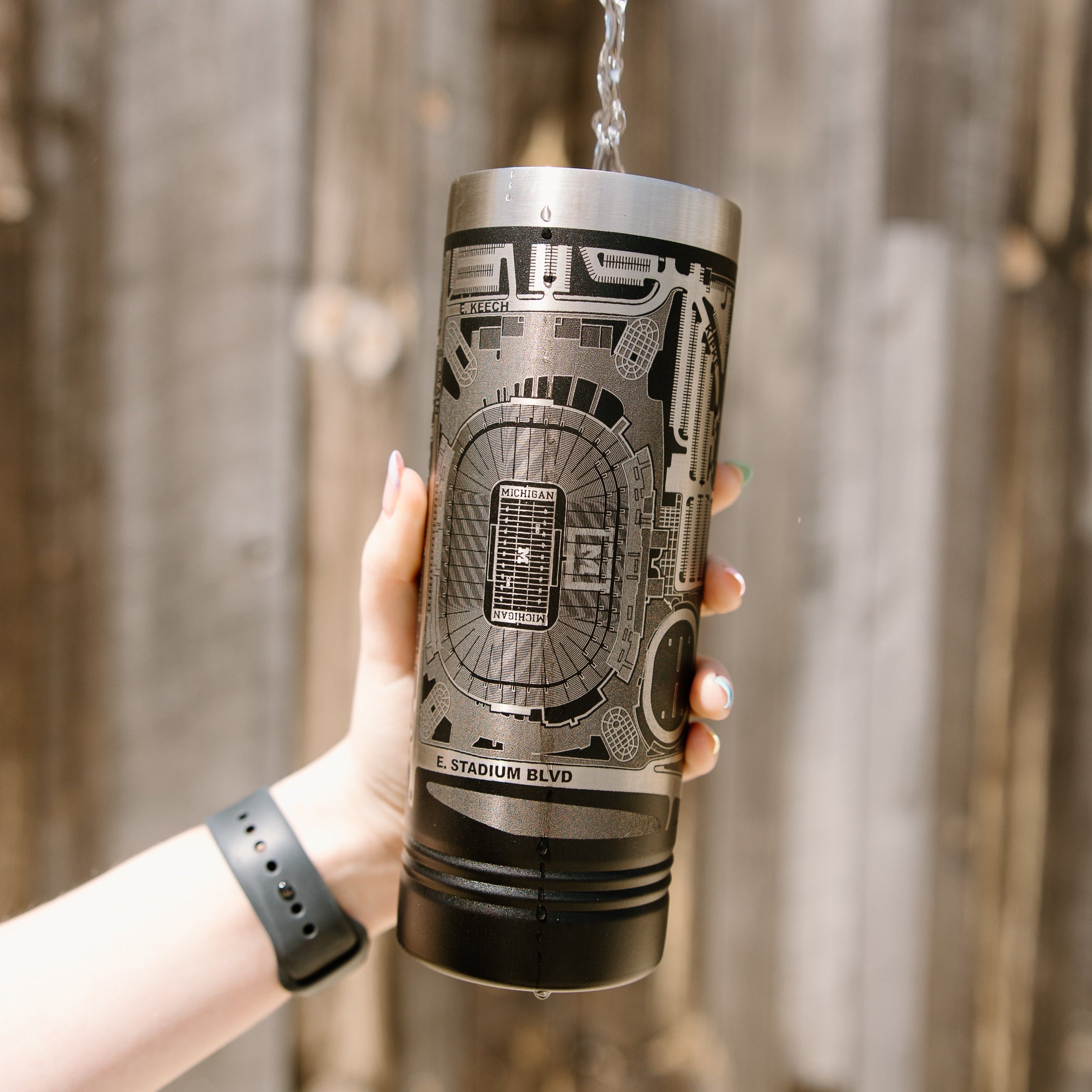 Person holding a black tumbler with a design against a wooden background